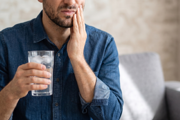 A man holding a glass of iced water while clutching his cheek in pain, indicating a severe toothache or temperature sensitivity.